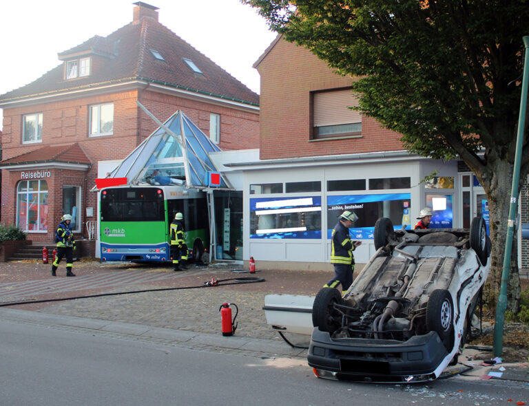 Auto over de kop en bus in reisbureau na aanrijding, buschauffeur zwaargewond